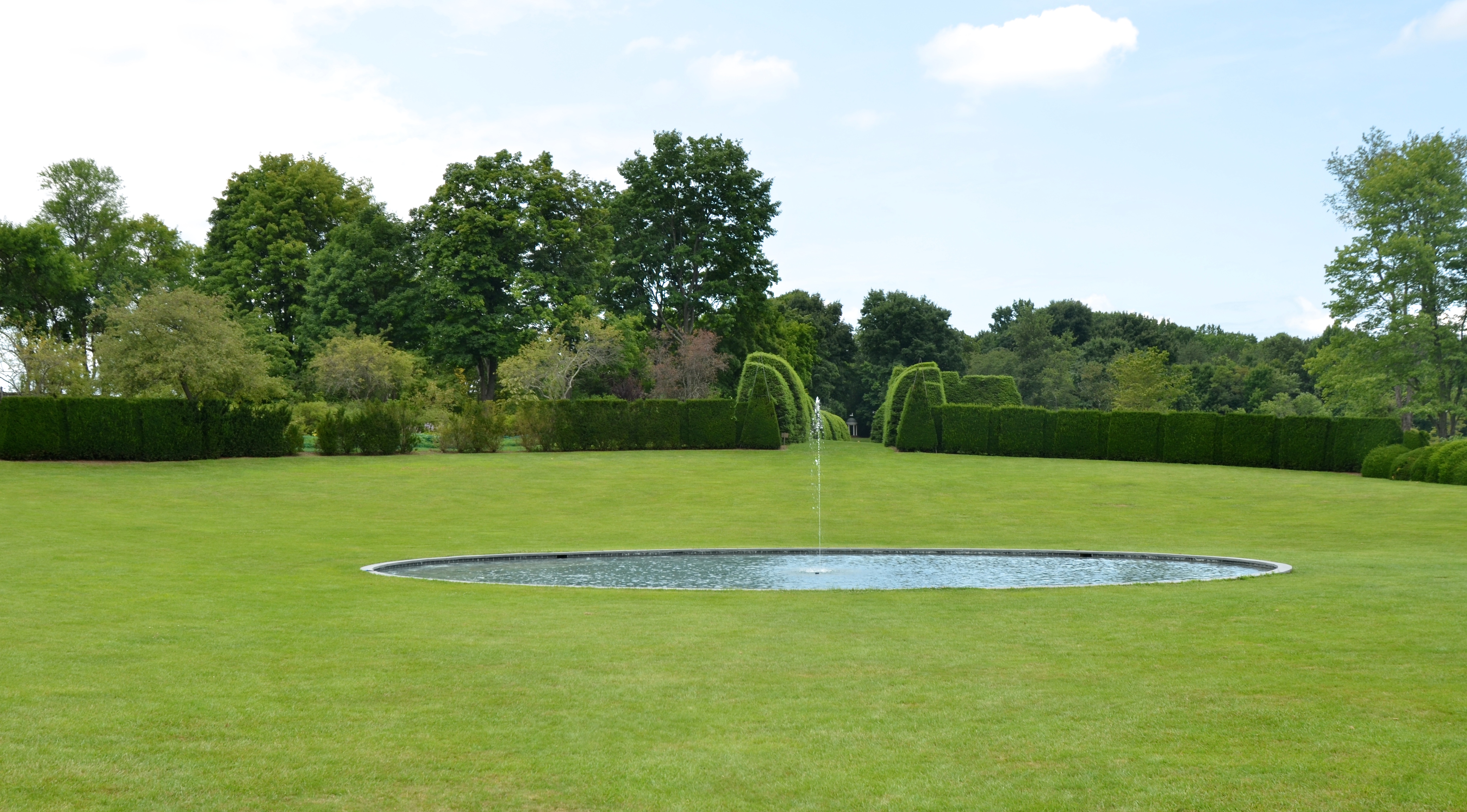 A tranquil oval pool reflects the sky in the center of the Great Bowl at Ladew Topiary Garden